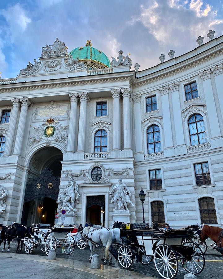 Sehenswürdigkeit Wiener Hofburg, Historische Burg der Habsburger Dynastie, Eingangsbereich mit historischer Fassade und Pferdekutschen im Vordergrund