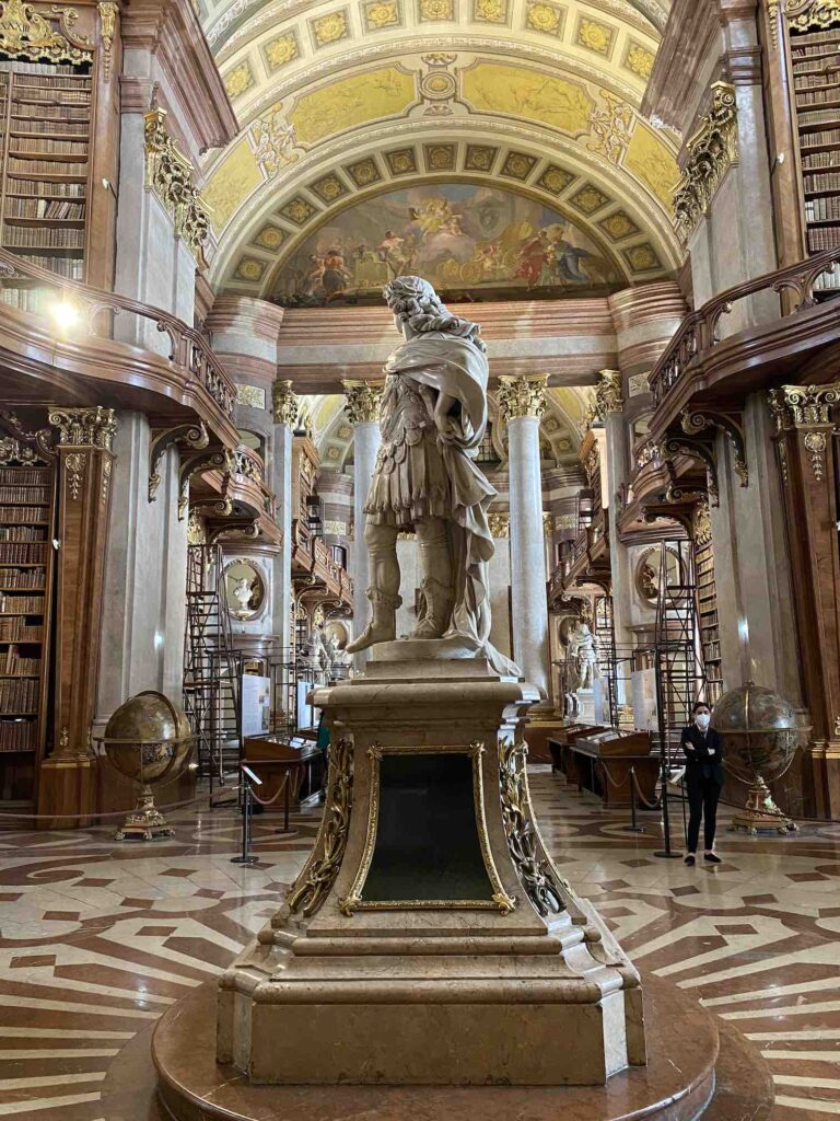 Blick in dien Prunksaal der Österreichische Nationalbibliothek, prunkvolle Ausstattung mit Deckenkuppel, Wandmalereien und Statue im Innenbereich